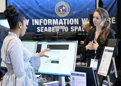 National Harbor, MD (Apr. 10, 2018) Christina Lewis, right, assigned to Space and Naval Warfare Systems Center Atlantic fields a question pertaining to Project Inquisitor, her advanced data analytics demonstration in the Navy Information Warfare Pavilion at the 2018 Sea, Air and Space exposition (SAS). The Information warfare pavilion is presented by a partnership between the Office of the Deputy Chief of Naval Operations for Information Warfare (OPNAV N2N6); Commander, U.S. Fleet Cyber Command/Commander, U.S. 10th Fleet (CFCC/C10F); Space and Naval Warfare Systems Command (SPAWAR) and Commander, Naval Information Forces (NAVIFOR), all key players in the Navy™s Information Warfare community. SAS, sponsored by the U.S. Navy League, is the world™s largest maritime exposition and provides a venue of interaction between the maritime defense industry and U.S. and international military organizations. U.S. Navy photo by Rick Naystatt